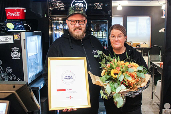 JJ'S BBQ omistama pariskunta hymyilemässä diplomin ja kukkakimpun kanssa