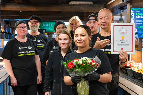 Ravintolan henkilökunta hymyilemässä buffetpöydän edessä kukat ja diplomi kädessä